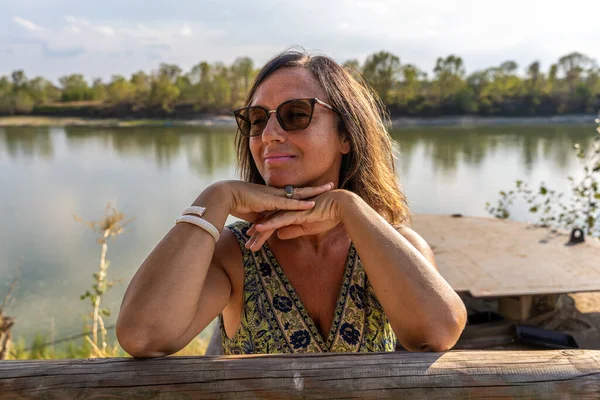 portrait of beautiful middle aged lady wearing sunglasses on the banks of the river at sunset
