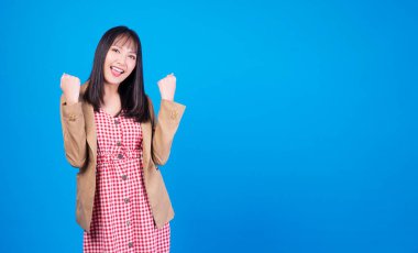 Yaşam tarzı, kazanan konsept. Olumlu gülümse mutlu iş kadını yumruğunu başarıyla tutarken mi yoksa mavi arka planda dikilirken mi şanslısın.