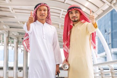 Takım çalışması başarılı bir konsept. İki ortak Arap Müslüman işadamı, toplantı sonrasında başparmaklarını kaldırarak başörtüsü takıyor. Şehir merkezinde birlikte dururken iş konuşuyorlar..