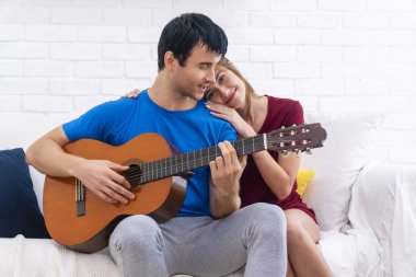 Yaşam tarzı ilişkisi ya da sevgi dolu bir kavram. Evdeki beyaz koltukta birlikte otururken akustik gitar çalan neşeli bir çift. Yakışıklı adam kendi kız arkadaşı için şarkı söylüyor..