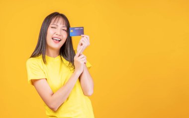 Ödeme ve finansal konsept. Neşeli genç bir kadın, günlük kıyafetler giyip elinde kredi kartı maketi tutarken izole edilmiş sarı arka planda fotokopi aletiyle dikiliyor.. 