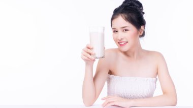 Beyaz arka planda beyaz masada otururken, sağlıklı bir cilt için bir bardak taze süt içen sevimli, ince Asyalı kadın. Formda vücut konsepti için sağlık hizmetleri kalsiyum gıdası.