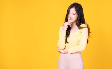 Kendine güvenen çekici Asyalı genç kadın, izole edilmiş sarı arka planda duran hipster tarzı giyiniyor. Neşeli öğrenci ya da iş kadını kameraya bakarken akıllı başarı.