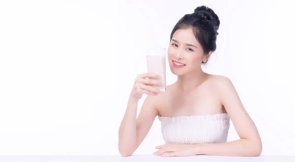 白いテーブルの上に孤立した白い背景の上に座っている間 健康的な肌のための新鮮なミルク飲料のガラスを保持魅力的なスリムアジアの女性 体のコンセプトに合った健康管理カルシウム食品 — ストック写真