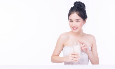 Beyaz arka planda beyaz masada otururken sağlıklı bir cilt için cam gibi taze süt içen sevimli ince Asyalı kadın. Formda vücut konsepti için sağlık hizmetleri kalsiyum gıdası.