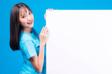 Heyecanlı Asyalı kadın beyaz afiş üzerinde sunum yapıyor. Boş fotokopi alanı, izole edilmiş mavi arka planda duruyor. Pankart, reklam, tabela sunum konsepti sergileyen Asyalı genç kız..