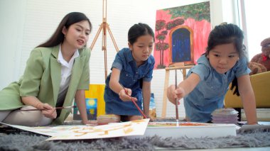 Asian two siblings learning study watercolor paint together at home. Teacher or parent teach student or daughter drawing paint color imagination on paper homework.Activity creativity education concept