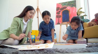 Asian two siblings learning study watercolor paint together at home. Teacher or parent teach student or daughter drawing paint color imagination on paper homework.Activity creativity education concept