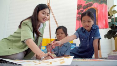 Asian two siblings learning study watercolor paint together at home. Teacher or parent teach student or daughter drawing paint color imagination on paper homework.Activity creativity education concept
