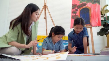 Asian two siblings learning study watercolor paint together at home. Teacher or parent teach student or daughter drawing paint color imagination on paper homework.Activity creativity education concept