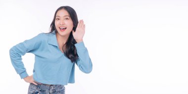 Excited asian woman holding hand beside ear listening something on white background. Confidential young girl listen news or gossip copy spaced over isolated background. Advertisement shopping concept.