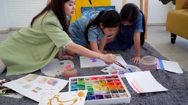 Asian two siblings learning study watercolor paint together at home. Teacher or parent teach student or daughter drawing paint color imagination on paper homework.Activity creativity education concept