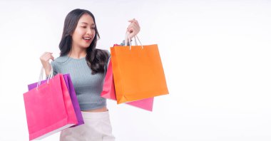 Enjoyment excited asian woman carry shopping bags standing on white background. Trendy happy shopper consumer carefree young girl looking shopping paper bags with copy space over isolated background.