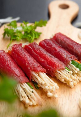 Grilled beef meat rolls with bell peppers, enoki mushrooms, carrots, tomato,  bowls, and plates with food top view
