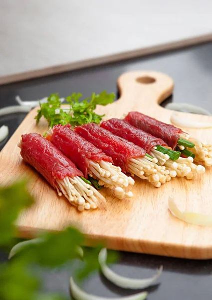 Grilled beef meat rolls with bell peppers, enoki mushrooms, carrots, tomato,  bowls, and plates with food top view