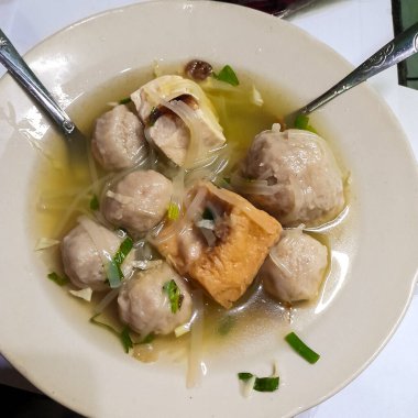 tasting the savory menu of fresh beef meatballs that are halal in Indonesia. consisting of beef meatballs, vermicelli noodles, scallions, fried onions, fried tofu, and a savory hot sauce.