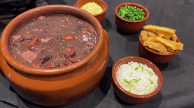 Delicious feijoada bowl with side dishes. Brazilian typical cuisine made with black beans. Visible smoke.