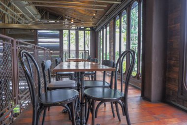 Siyah sandalye ve masa. Zemin eski bir kalas. Demir çit ve cam pencereler, klasik tarzda..