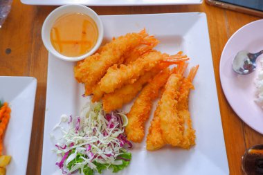 Dayak yemiş karides kuyrukları ve kızarmış ekmek kırıntıları beyaz bir tabağa konur, sosla servis edilir, doğranmış marul.