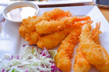 Dayak yemiş karides kuyrukları ve kızarmış ekmek kırıntıları beyaz bir tabağa konur, sosla servis edilir, doğranmış marul.