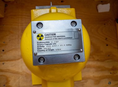 İsim levhasındaki radyasyon uyarısı fabrika işlem aletinin mekanik konteynırı arka plan olarak radyasyon tehlike sembolünü iyonlaştırıyor.