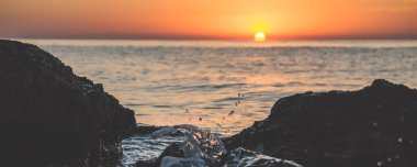 Sea waves breaking on a rocky shore against the backdrop of the setting sun