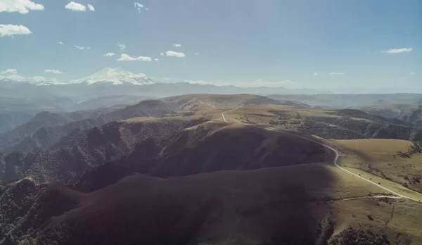 Shooting from a quadrocopter with a view of the Caucasus mountains and the ridge, the white peak of Mount Elbrus stands out, in the foreground below is the road along the mountain ridge