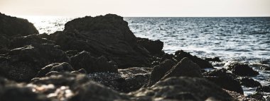 Deniz kıyısındaki karanlık kasvetli kayalar ve kayaların üzerindeki Karadeniz 'in çarpan dalgaları, kayaların ve deniz ufkunun panoramik manzarası.