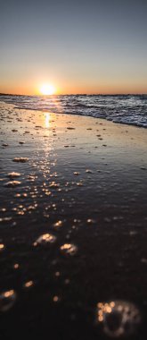 Sıcak turuncu günbatımı güneşi, Karadeniz kıyılarındaki kıyı dalgasının ayna yüzeyine yansıyor. Akşamları dikey olarak.