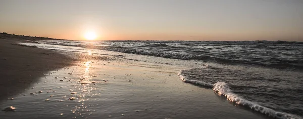 Panoramic warm evening sunset on the Black Sea coast with waves and foam of violent waves, warm summer evening