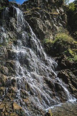 Soğuk bir dağ şelalesinin dereleri dağın kayalıklarından taşar ve sıcacık bir sonbahar gününde su sıçrar.
