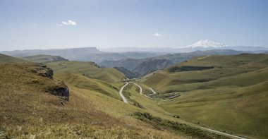 Kafkasya 'nın dağ tepeleri ve dağ yamaçlarında dağ kıvrımlı yolları olan kayalar Elbrus Dağı' nın arka planında karla kaplı.