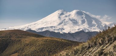 Elbrus Dağı 'nın iki zirvesi ve çevresindeki dağ manzarası, Ekim ayında Kafkasya' da, ılık sarı sonbahar renklerinde, pohpohlayıcı bir diziye sahiptir.
