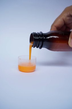 Kadın eli, beyaz arka planda ölçme kabına öksürük şurubu döker. Sağlık kavramı