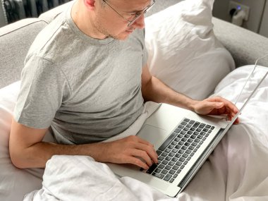 Middle aged adult man using laptop at home In bed vibes white bedsheets Alone Early morning working. freelancer, freelance job, using technology, using social media, watching movie, checking news