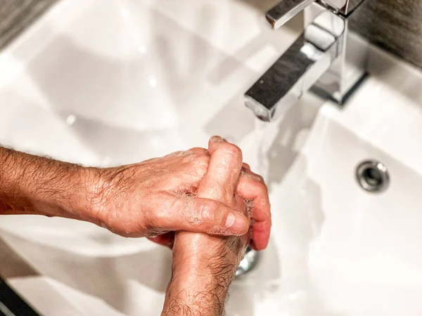 Personal hygiene: man is washing hands with soap properly at home.