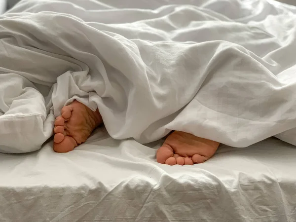 View of male feet, man sleeping at home. Middle aged adult man is sleeping at home. Cozy bedroom vibes. White bedsheets, bed linen, alone, early morning atmosphere.