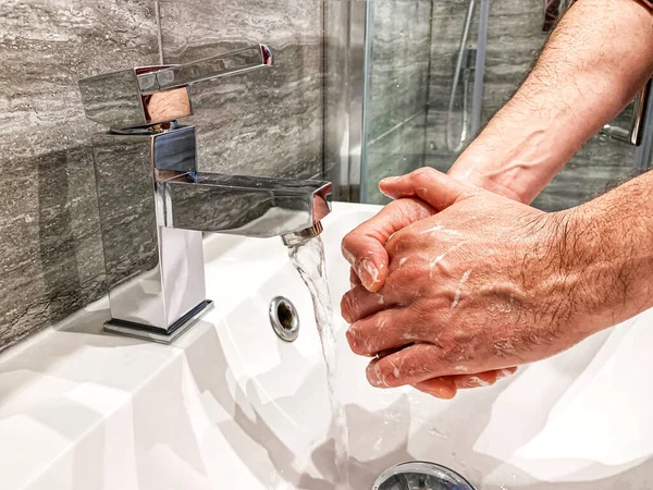 Personal hygiene: man is washing hands with soap properly at home.