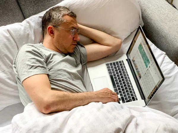 Middle aged adult man using laptop at home In bed vibes white bedsheets Alone Early morning working. freelancer, freelance job, using technology, using social media, watching movie, checking news