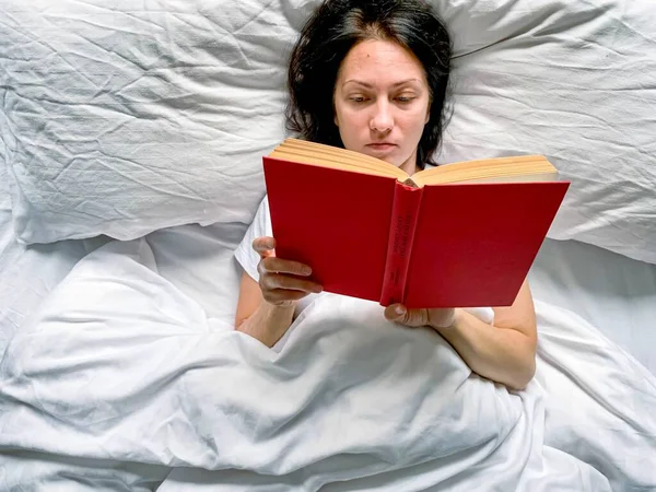 Young Millennial Candid Woman Reading Red Book Home White Striped Rechtenvrije Stockafbeeldingen