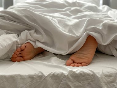 View of male feet, man sleeping at home. Middle aged adult man is sleeping at home. Cozy bedroom vibes. White bedsheets, bed linen, alone, early morning atmosphere. 