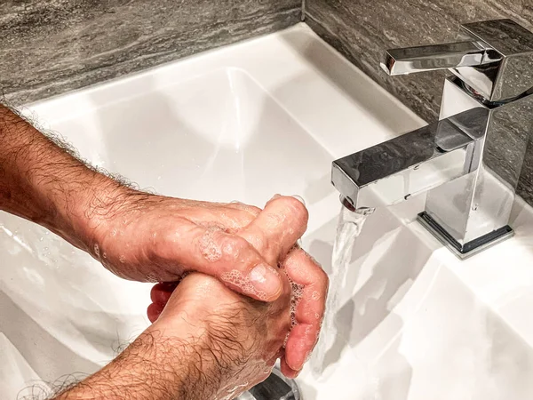 Personal hygiene: man is washing hands with soap properly at home.