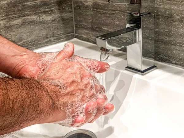 Personal hygiene: man is washing hands with soap properly at home.
