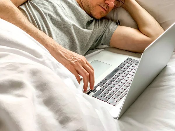 Middle aged adult man using laptop at home In bed vibes white bedsheets Alone Early morning working. freelancer, freelance job, using technology, using social media, watching movie, checking news