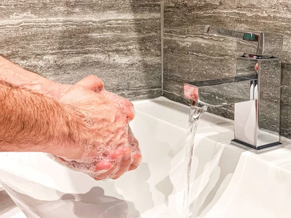 Personal hygiene: man is washing hands with soap properly at home.