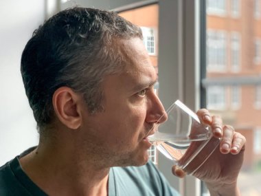 Orta yaşlı adam susuz kalmak için su içiyor. Susamış adam akşamdan kalma, saf su içiyor.