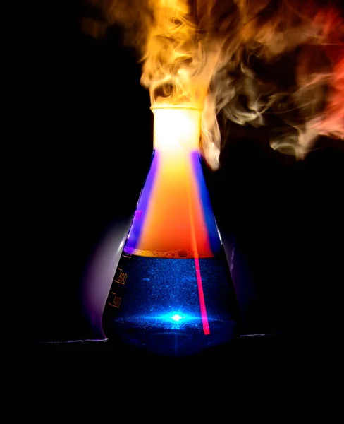 Strong chemical reaction with a lot smoke and vapors inside Erlenmeyer flask. Ignition is starting. Vessel with a blue liquid is standing on the table. . High quality photo