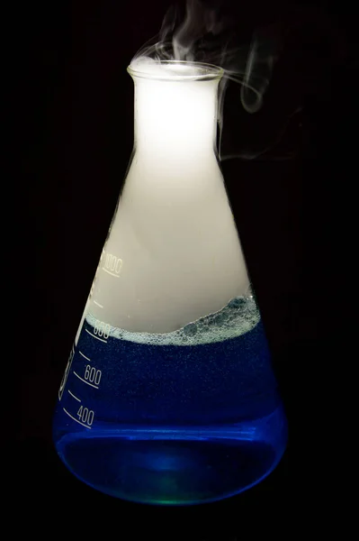 Erlenmeyer flask with a blue liquid and smoke which has been created by a chemical reaction. Background picture. . High quality photo