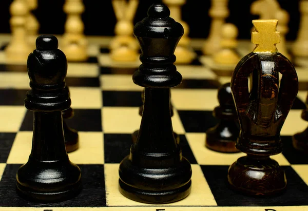 Black king, queen and bishop are standing in a row on a chessboard. Dark background. . High quality photo