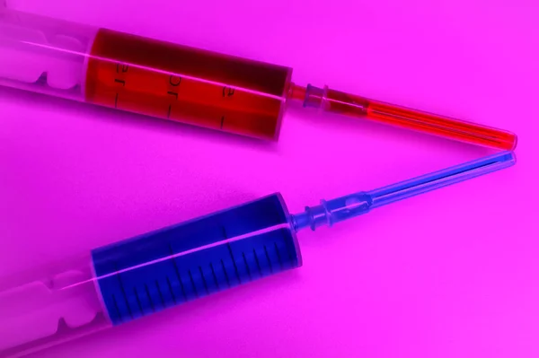 Two medical syringes one with the vaccine and one with the test blood on purple background. . High quality photo
